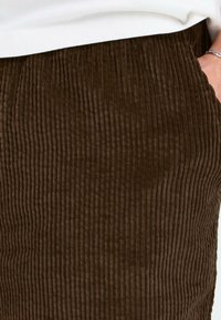 Brown corduroy pants with vertical ribbed texture, featuring side pockets and a soft fabric finish.