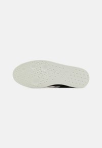 Semelle d'une chaussure blanche avec des motifs circulaires et triangulaires texturés et le mot « ecco » embossé près de la zone de la voûte plantaire.