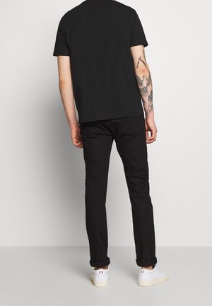 Camiseta de algodón negra con un corte holgado, combinada con vaqueros negros. Zapatillas blancas de diseño minimalista y puños doblados completan el atuendo.