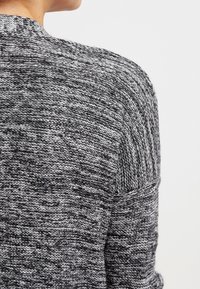 Sweter rozpinany wykonany na drutach, z teksturowanym wzorem w odcieniach szarości i czerni, z okrągłym dekoltem i szerokim panelem na plecach.