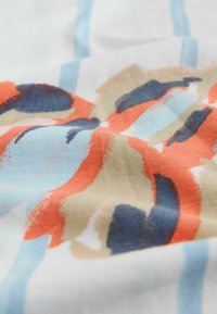 Blødt stof med abstrakt penselstrøgsmønster i orange, marineblå, beige og lyseblå på hvid baggrund.