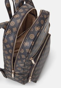 Petit sac à dos marron foncé avec motif monogramme beige, deux compartiments zippés partiellement ouverts et bretelles ajustables.