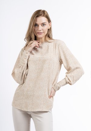 Blusa a maniche lunghe beige con un piccolo motivo a pois bianchi. Presenta un collo arrotondato, maniche a palloncino e polsini con bottoni. Tessuto morbido.