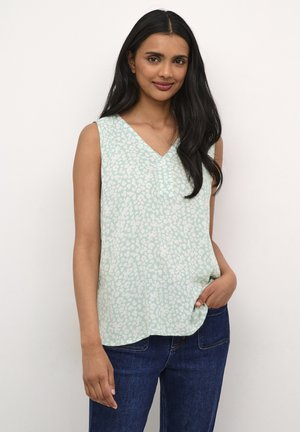 Haut sans manches vert clair avec décolleté en V, présentant un motif floral subtil et une coupe ample et fluide. Associé à un jean en denim bleu foncé.