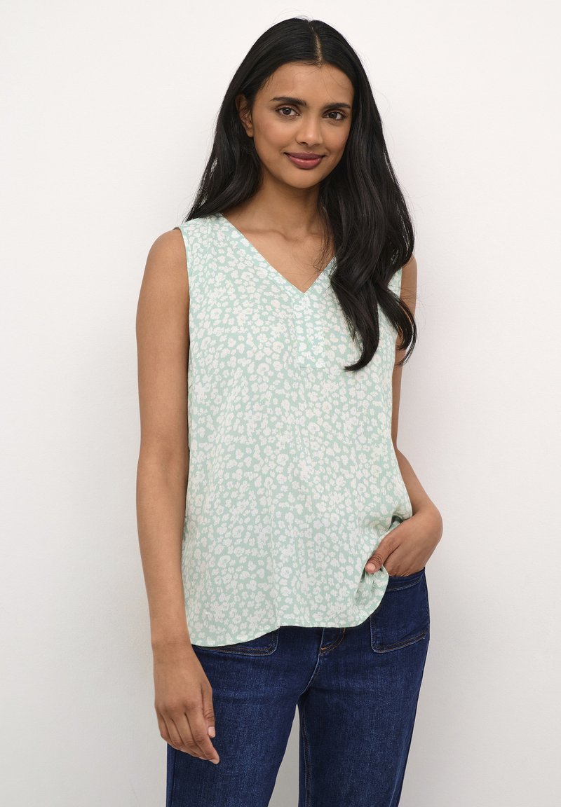Top verde deschis fără mâneci, cu un gât în formă de V, având un model floral subtil și un design lejer, fluid. Asortat cu blugi din denim albastru închis.