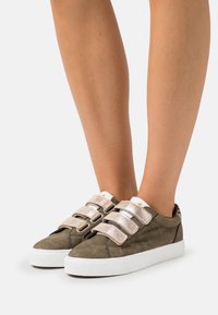 Green suede sneakers with three metallic silver Velcro straps, white rubber sole, and minimal design. Suitable for casual wear.