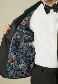 Fekete szmoking zakó színes paisley mintás szatén béléssel; oldalsó zseb és 'NEXT SLIM FIT' címke jellemzi.