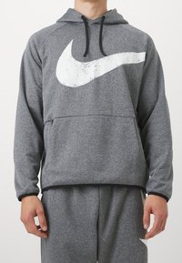 Sweat à capuche gris avec un grand logo Nike blanc vieilli. Comprend une poche kangourou frontale et une capuche à cordon. Texture lisse.
