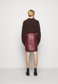 Brauner Strickpullover, dunkelroter Bleistiftrock aus Leder und schwarze Stiefeletten. Der Pullover ist cropped geschnitten; der Rock hat eine glatte Textur und Naht-Details.