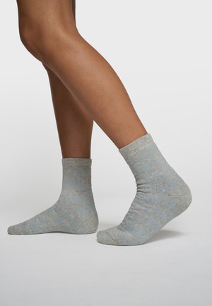 Benen met lichtgrijze enkelsokken met een blauw tekstpatroon met woorden zoals "LOVE" en "SMILE", tegen een effen witte achtergrond.