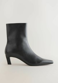 Stivale alla caviglia in pelle nera con un design elegante e aderente, punta appuntita e tacco a blocco piccolo, caratterizzato da una texture liscia e dettagli minimi.