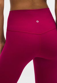 Dopasowane legginsy o wysokim stanie w jaskrawym fuksjowym kolorze, z gładką teksturą i subtelnym logo z tyłu. Szwy materiału są przeszywane, a materiał jest elastyczny.