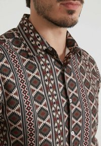 Chemise à manches courtes avec un motif géométrique dans des teintes terreuses, dotée d'un col boutonné et fabriquée dans un tissu léger et texturé.