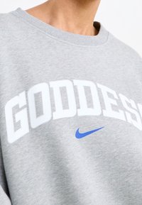 Felpa grigia con grande scritta bianca "GODDESS" e logo blu Nike. Tessuto morbido con scollatura rotonda e polsini a costine.
