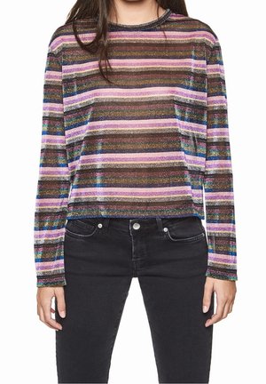 Femme portant un haut à manches longues rayé horizontal multicolore avec des paillettes et un jean noir taille haute.