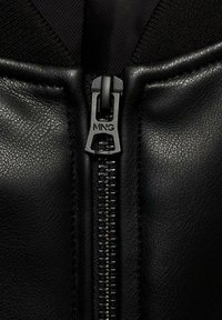 Gros plan sur une fermeture éclair d'une veste en cuir noire avec des panneaux en cuir texturé et "MNG" embossé sur le tire-zip.