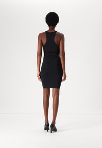 Μαύρο χωρίς μανίκια φόρεμα bodycon με εφαρμοστό σχέδιο και κοπές στη μέση, σε συνδυασμό με μαύρες ψηλές γόβες.