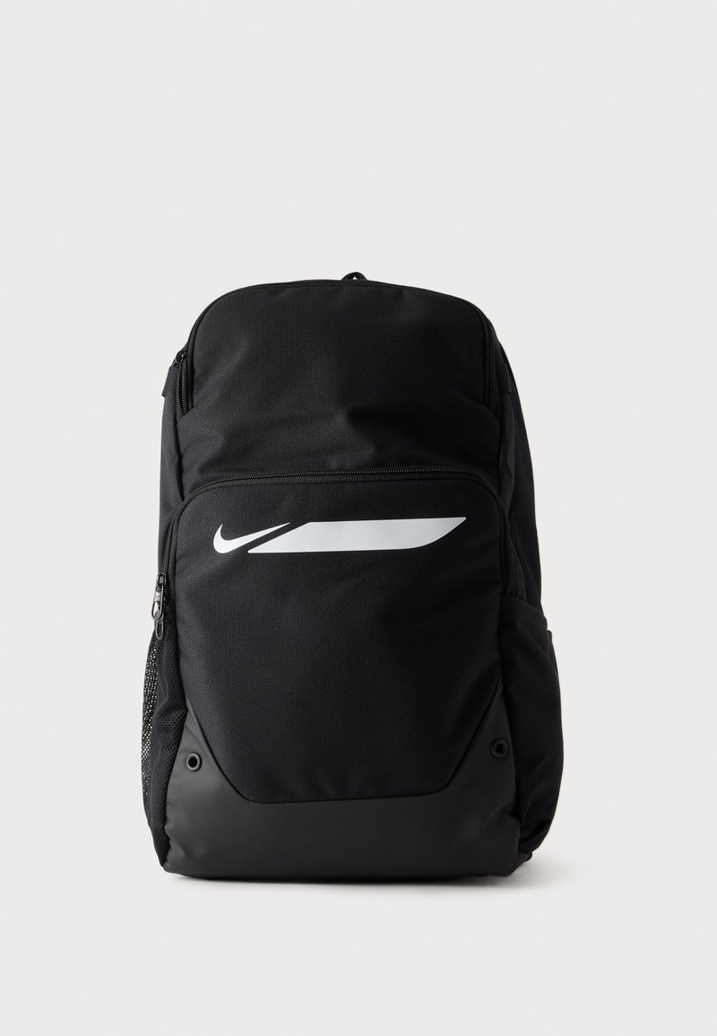 Μαύρο σακίδιο Nike με μπροστινή τσέπη με φερμουάρ, λευκό λογότυπο swoosh και δίχτυ στην πλαϊνή τσέπη σε απλό φωτεινό φόντο.