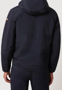 Giacca a vento blu navy con cappuccio realizzata in tessuto leggero, caratterizzata da una superficie liscia e un'etichetta con logo sulla spalla.