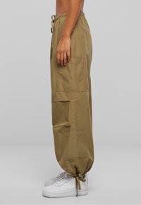 Beige cargobukser med sidelommer, samlede nederste kant og snor i livet, kombinert med hvite joggesko. Glatt tekstur, løs passform.