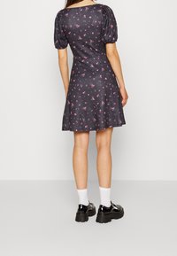 Černé šaty s krátkými nafouknutými rukávy a rozšířenou sukní, zdobené růžovým květinovým vzorem. Modelka má na sobě černé platformové boty a bílé ponožky.