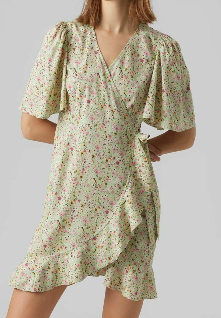 Robe portefeuille fleurie vert clair, avec manches courtes bouffantes, ourlet à volants et taille nouée. Le tissu présente un motif délicat et texturé.