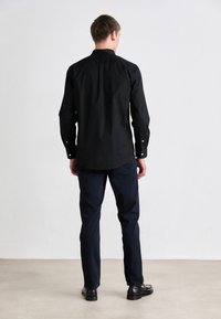 Black long-sleeve shirt with a button-down collar, paired with dark navy pants. The shirt features a smooth texture and minimalistic design.