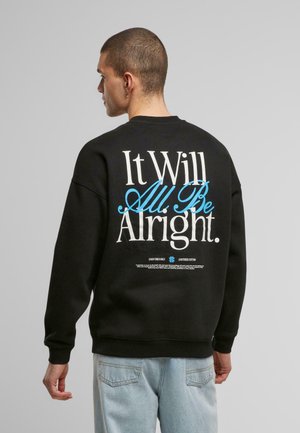 Sudadera negra con gran texto en la parte posterior que dice "Todo estará bien". Cuello redondo, puños y dobladillo acanalados. Ajuste casual.