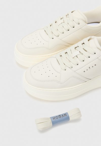 Baskets en cuir blanc avec perforations, bout rond, semelle épaisse et lacets beige. Comprend des lacets de rechange enveloppés dans une étiquette bleue portant la mention "Hogan."