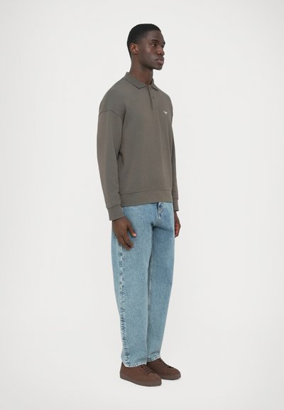 Πράσινο χακί πλεκτό πόλο με άνετη εφαρμογή, συνδυασμένο με ανοιχτό μπλε τζιν παντελόνι κανονικής γραμμής και καφέ δερμάτινα παπούτσια με κορδόνια. Απλή λεπτομέρεια λογότυπου στο στήθος.