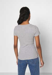 Camiseta gris claro con textura acanalada, mangas cortas, diseño ajustado y cuello redondo, combinada con vaqueros azules de talle alto.