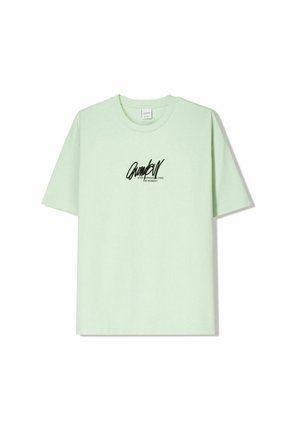 T-shirt in cotone verde chiaro con maniche corte, colletto tondo e stampa grafica nera sul petto. Tessuto morbido e vestibilità rilassata.