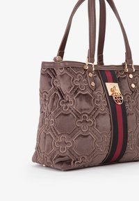 Bolsa de tela marrón con patrón floral en relieve, herrajes dorados y un acento a rayas rojas y negras en el lateral. Incluye doble manejo.