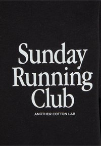 Black cotton fabric displaying "Sunday Running Club" in large white font, with smaller text "ANOTHER COTTON LAB" underneath.