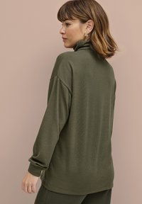 Olijfgroen pullover met een hoge hals, verlaagde schouders en lange mouwen. Zachte textuur met een relaxte pasvorm en geribbelde manchetten.