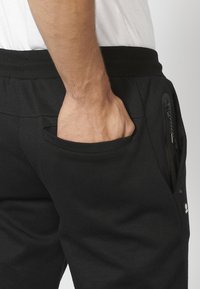Sorte sweatpants med strikket talje, sidelomme med lynlås, glat tekstur og slim fit design.
