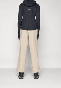 Lightweight black hoodie with a fitted design, beige loose-fitting pants, and black hiking boots. Features logo on the upper back.