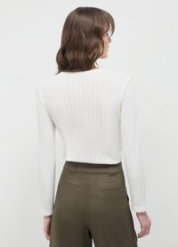 Maglione bianco a coste con maniche lunghe, caratterizzato da un colletto rotondo e un tessuto texturizzato, abbinato a pantaloni verde oliva a vita alta.