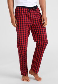 Pantalones de pijama a cuadros rojos y azul marino hechos de una tela ligera, con cinturilla elástica, cordón ajustable y un cierre de botón.
