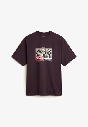 Purple cotton t-shirt featuring a graphic print centered on a group of spray paint cans, bordered by red and white text details.
