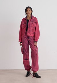 Veste en denim rose vif et pantalon cargo avec une texture légèrement délavée. Comprend des poches, des poignets et une coupe décontractée. Des bottes noires complètent le look.