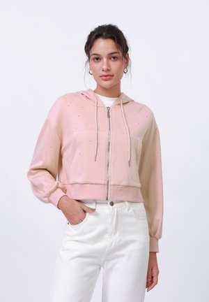 Geknipte roze hoodie met een metallic glans, voorrits, trekkoord capuchon en twee zijzakken, gecombineerd met witte high-waist jeans.