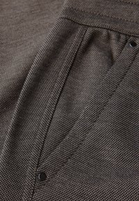 Tissu marron avec un tissage texturé et à motifs ; présente un design en v distinct et un petit détail de bouton noir.