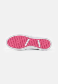 Sola di sneaker bianca con inserto rosa a contrasto che presenta il marchio "TOMMY JEANS" ripetuto. Superficie testurizzata e liscia con ritagli.