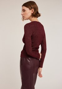 Mörkröd randig topp med långa ärmar, figurnära design och texturerad yta. Kombination med en högmidjad läderkjol som framhäver en elegant silhuett.