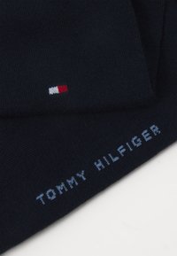 Marinblå stickad mössa med en liten röd, vit och blå logotyp, med "TOMMY HILFIGER" broderad i ljusblått. Mjuk känsla.
