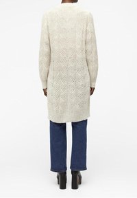 Cardigan long en maille beige clair avec un motif de feuilles texturé, coupe droite, manches longues et ourlet arrondi.