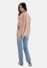 Ljust rosa texturerad tröja med långa ärmar, rund halsringning och lös passform, parat med ljusblå jeans och vita sneakers.