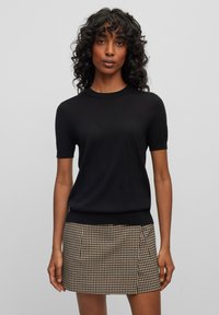 Maglione nero a maniche corte realizzato in un materiale morbido, con scollatura rotonda e orlo aderente. Abbinato a una mini gonna a quadri marrone.