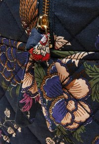 Pikowana torba z tkaniny o granatowym tle i żywych kwiatowych wzorach w kolorach fioletowym, czerwonym i zielonym, z złotym suwakiem i ozdobnym chwostem.